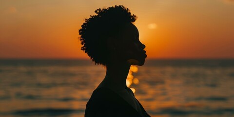 Silhouette of a woman with curly hair watching the sunset over the ocean