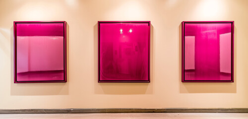 An avant-garde art gallery displaying three glossy magenta frames against a light cream wall, creating a playful and inviting environment