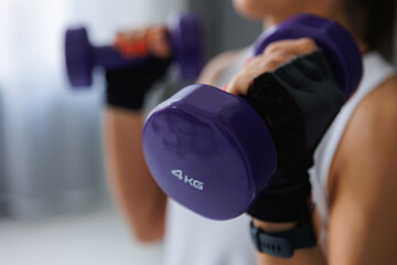 A woman in sports uniform is holding two purple dumbbells in her hands, showcasing her strength and...