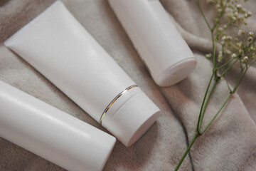Three white tubes of lotion are displayed on a rectangleshaped blanket next to a delicate flower,...