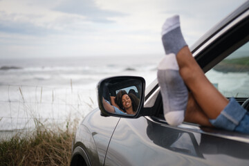 Cheerful woman resting and relaxing inside a car with her feet outside the window facing the sea....