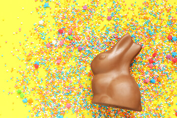 Chocolate bunny and colored sugar sprinkles on a yellow background, top view. Easter composition....