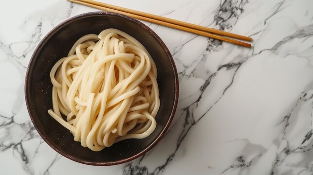 Dried udon nudles in a bowl closeup. Bunch of raw japanese vegan pasta from wheat flour and bamboo chopsticks over bowl against marble countertop.