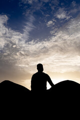 backlit shot of isolated man meditating at wall with sunset dramatic sky at dusk