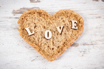 Wholegrain bread in shape of heart for breakfast and inscription love. Old rustic background