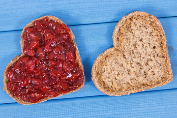 Slice of bread in shape of heart with strawberry jam for breakfast. Blue boards background