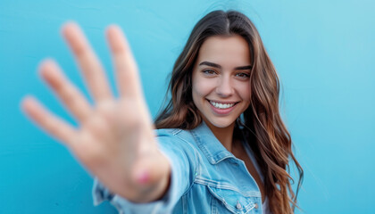 Fototapeta premium Happy young woman with brown hair in blue against a blue wall holding her hands up 