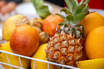 fruits, ripe pineapple, fresh oranges, and yellow bananas, arranged neatly in a wire basket,...