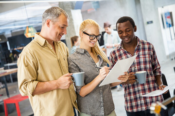 Three diverse colleagues discussing project with documents in modern office