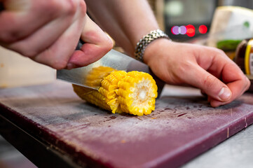 A person skillfully slicing fresh yellow corn on a wooden cutting board in a kitchen.