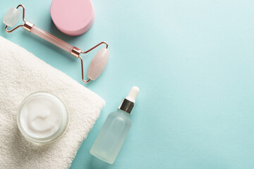 Skin care products. Cream jar, jade roller and serum bottle on blue background. Flat lay with copy...