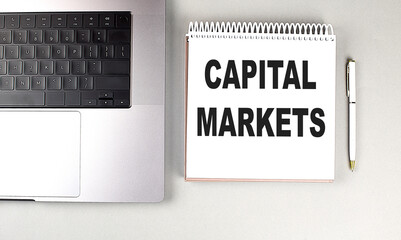 CAPITAL MARKETS text on notebook with laptop and pen