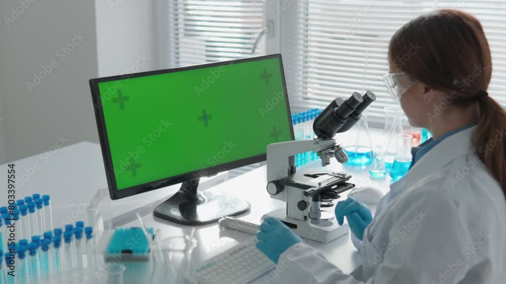 Poster Chroma key green screen. A laboratory where the scientist conducts research in the field of medicine and chemistry. Using a microscope, he studies biological structures, and using a computer, he