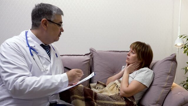 A male doctor is conducting an examination on a woman who complains of a sore throat. He is making notes in medical papers.