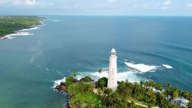 White colonial Dondra Head lighthouse surrounded by the ocean and palms on the jungle coast of Sri Lanka