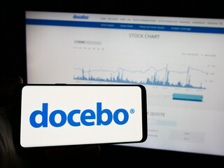 Naklejka premium Stuttgart, Germany - 04-17-2024: Person holding mobile phone with logo of Canadian learning software company Docebo Inc. in front of business web page. Focus on phone display.