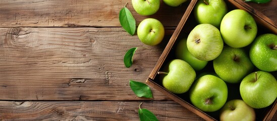 A wooden table with a box of green ripe apples on top, viewed from above and with room for text.