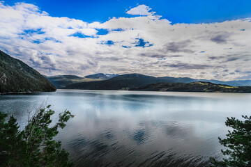 Serene view over Tingvollfjorden in Norway, featuring calm waters with reflections under a blue summer cloud sky.