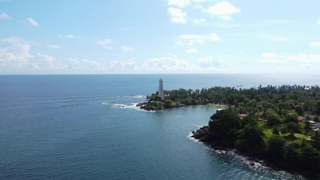 White colonial Dondra Head lighthouse surrounded by the ocean and palms on the jungle coast of Sri Lanka
