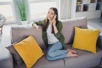 Full length portrait of nice young girl sit sofa speak phone wear green shirt modern interior flat...