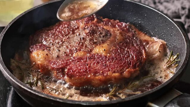 Chef pours melted butter on a juicy beef steak frying on a pan in the kitchen, close-up. Process of cooking delicious beef steak.