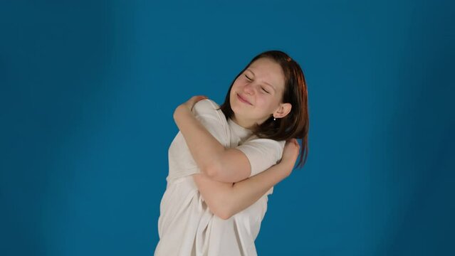 Lady embraces body with arms feeling happiness on blue background. Woman finds acceptance embracing every part with unconditional love slow motion