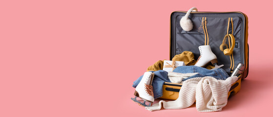 Suitcase with warm clothes, ice skates and Christmas gift box on pink background. Winter vacation...