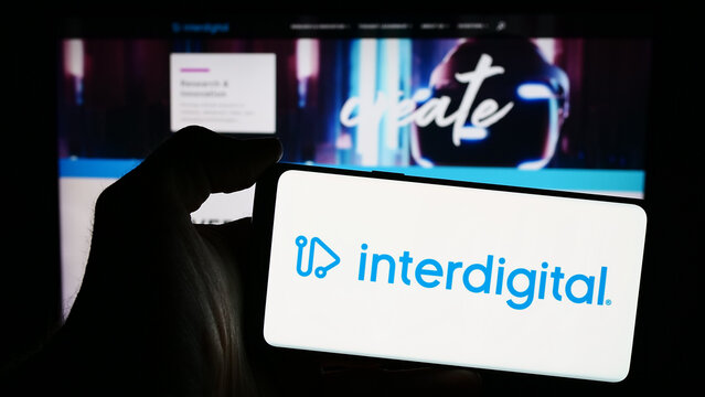 Stuttgart, Germany - 04-18-2024: Person holding mobile phone with logo of American technology company InterDigital Inc. in front of business web page. Focus on phone display.