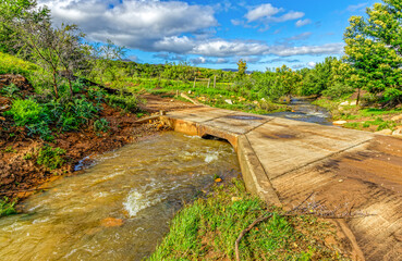 Strongly flowing stream running under low bridge following heavy rains in the Matjes River Valley near Oudtshoorn, Western Cape, South Africa