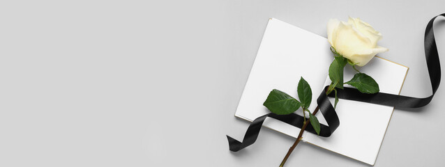 Rose with black ribbon and blank open notebook on white background