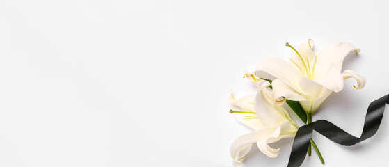 Beautiful lily flowers with black funeral ribbon on white background