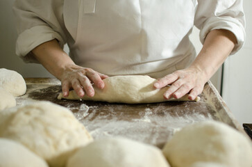 Handcrafting loaves of bread dough. Process occurs in a bakery. The dough is kneaded by warm hands.