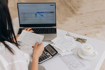 Back view of unrecognizable woman calculates utility expenses on laptop and calculator,doing online...