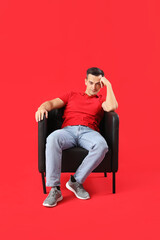 Handsome man sitting in black armchair on red background