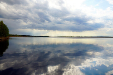 Beautiful clouds and blue sky over the lake. Reflection and horizon. Spring.