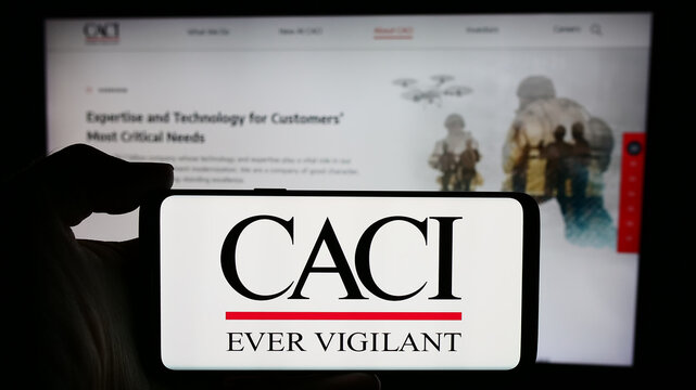 Stuttgart, Germany - 04-28-2024: Person holding cellphone with logo of US information technology company CACI International Inc. in front of webpage. Focus on phone display.