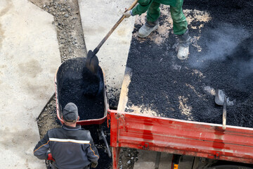 Road service workers unload fresh asphalt from a truck.