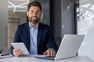 Confident businessman working with laptop and tablet in office