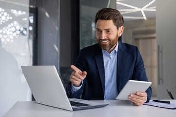 Confident businessman using laptop and tablet in office