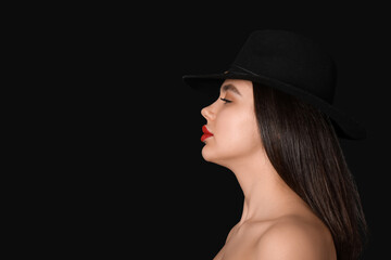 Beautiful young woman in hat with red lips on black background