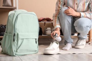Woman with bottle of water repellent spray, sneaker and backpack at home