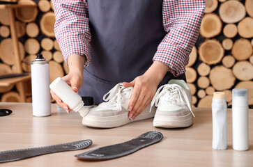 Female shoemaker cleaning stylish sneakers at wooden table, closeup