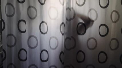 Silhouette of sensual woman taking a shower behind curtain with black and white circles on it. The curtain is partially covered by a person, slow motion - Powered by Adobe