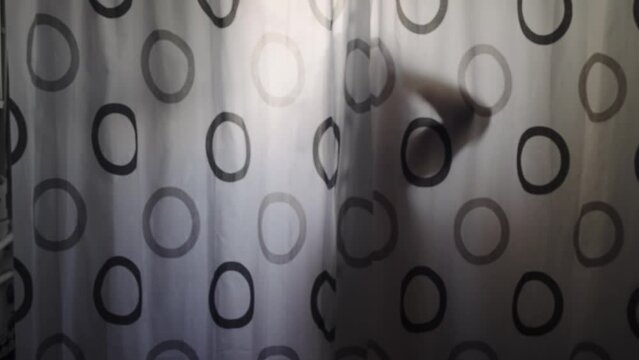 Silhouette of sensual woman taking a shower behind curtain with black and white circles on it. The curtain is partially covered by a person, slow motion