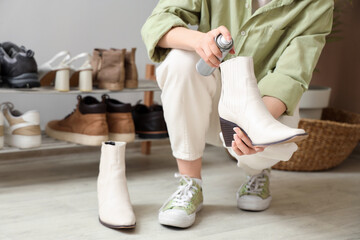 Woman applying water repellent spray on stylish shoes at home