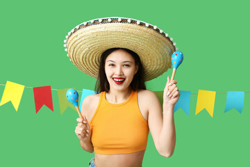 Happy young woman in Mexican sombrero hat, with maracas and garland on green background