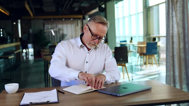 Irritated man sitting at desk pulls the page out of his notebook. Man grimacing much and puts the piece of paper to his mouth.
