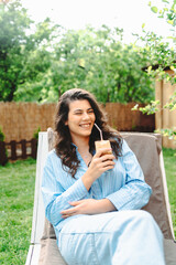 One young caucasian woman is relaxing on easy bed while drinking cold coffee in her backyard