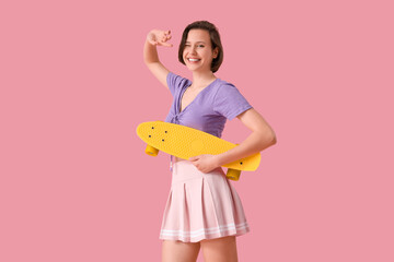 Happy young fashionable woman with skateboard on pink background