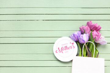 Greeting card with text HAPPY MOTHER'S DAY and beautiful tulips on green wooden background